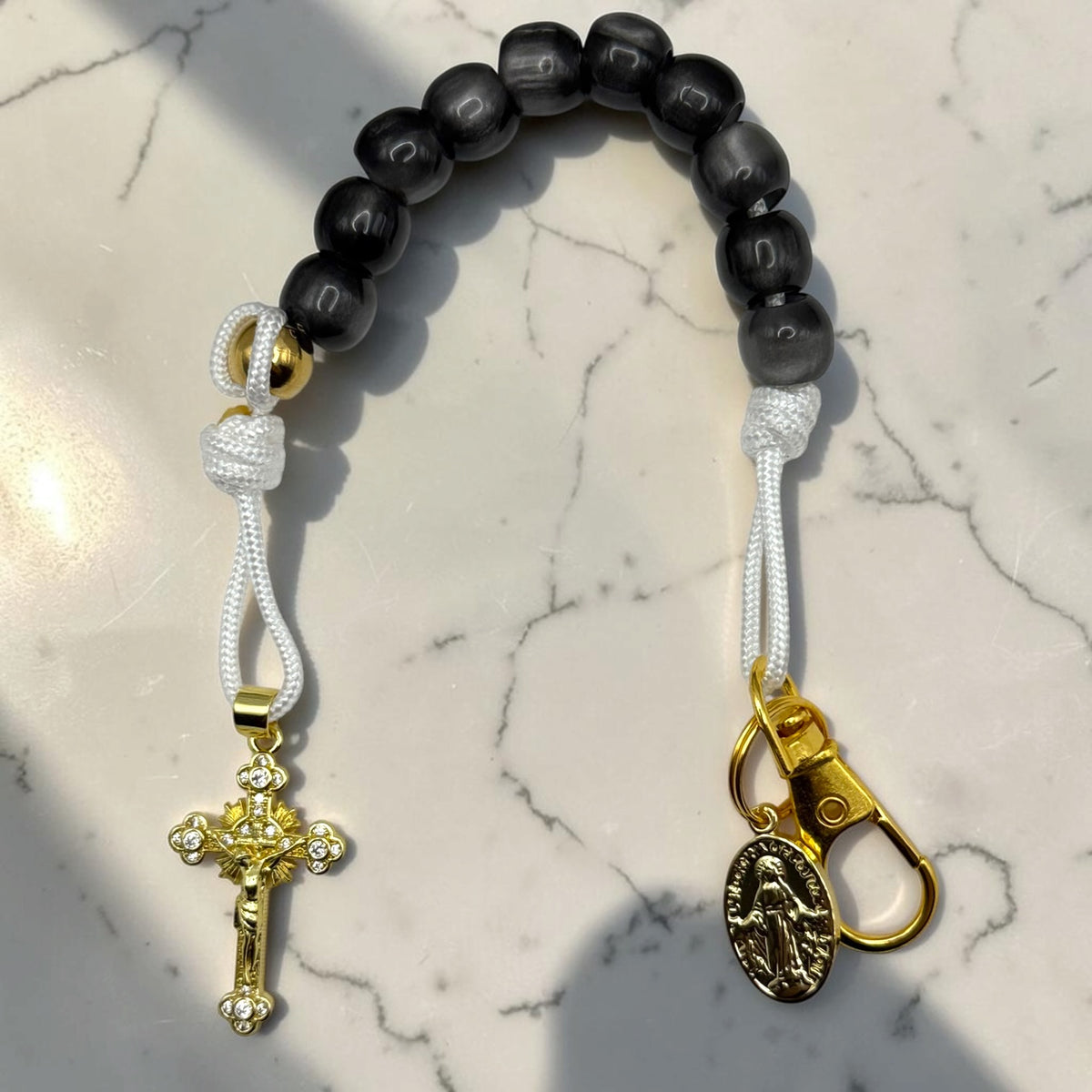 Black decade rosary with white cord, gold-tone hardware, Marian medal, and crystal crucifix