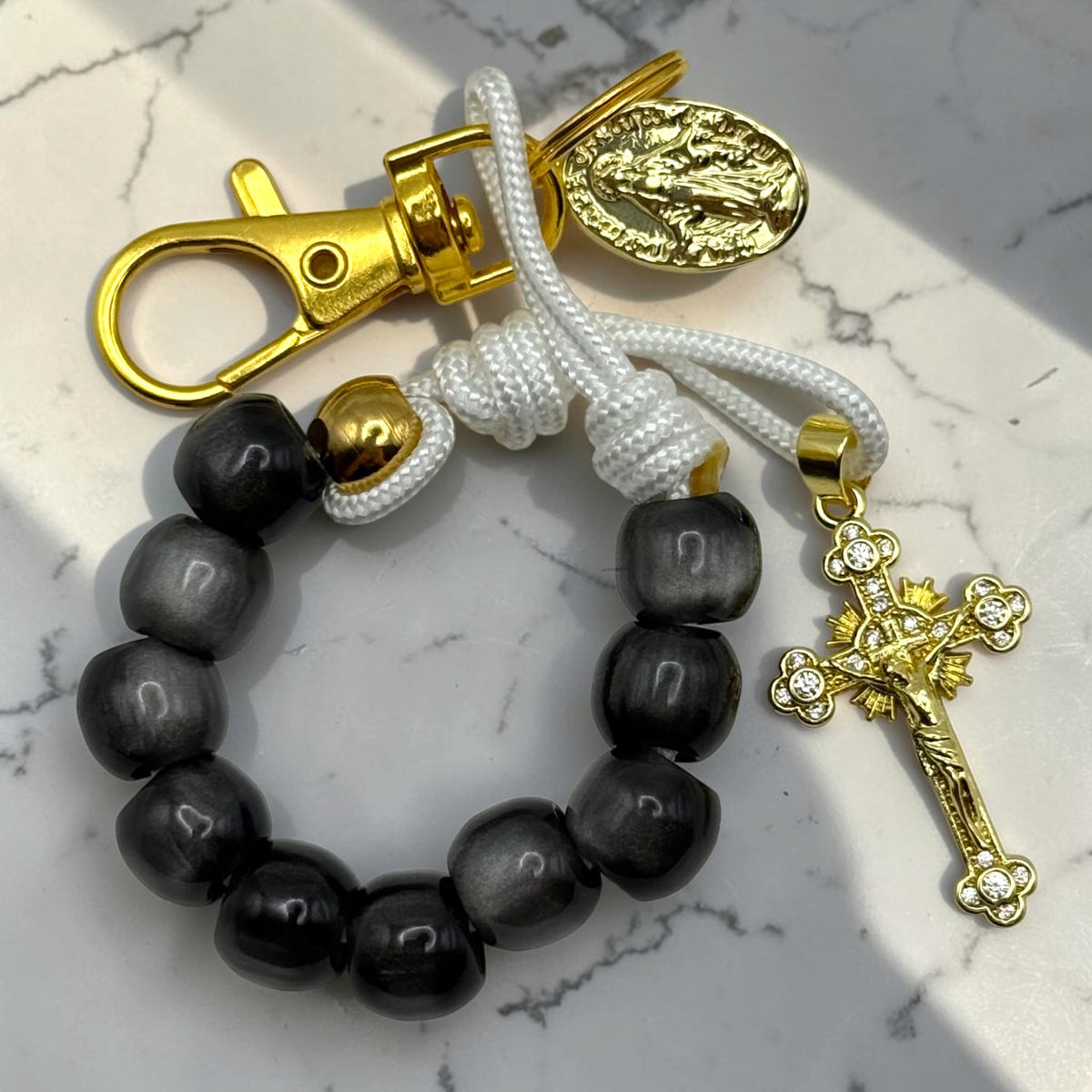 Close-up black decade rosary with white cord, gold-tone clasp, Marian medal, and crystal-accented crucifix