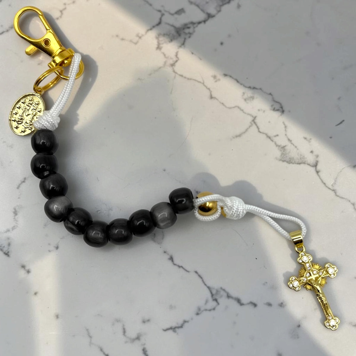 Full-length black decade rosary with white cord, gold-tone hardware, Marian medal, and crystal-accented crucifix