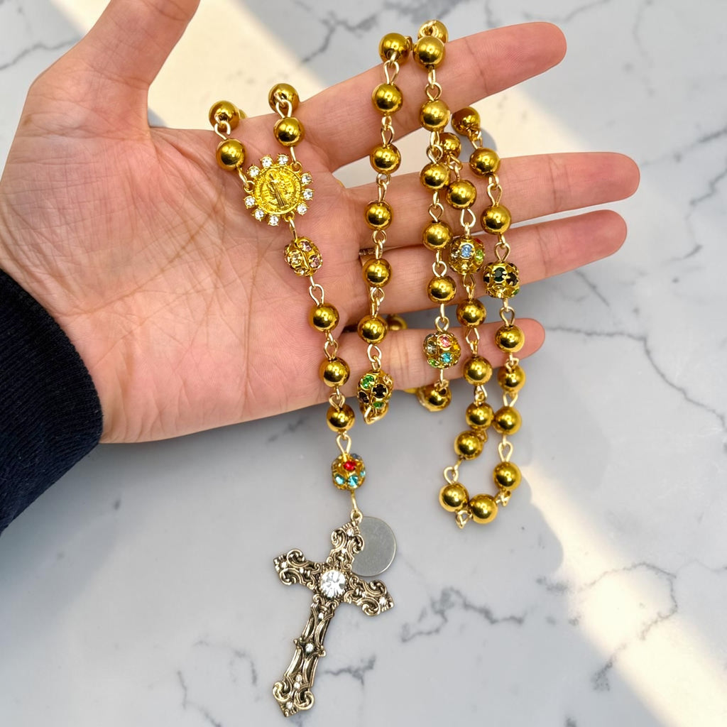 Gold Saint Benedict rosary shown in hand with crystal accents