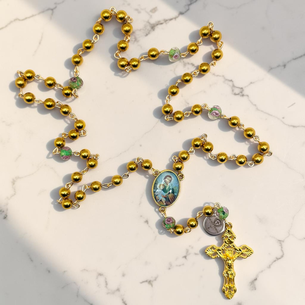 Gold Saint Joseph rosary laid out with floral glass Our Father beads