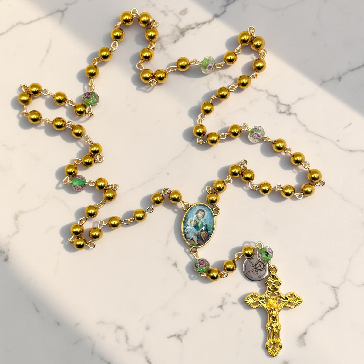 Gold Saint Joseph rosary laid out with floral glass Our Father beads