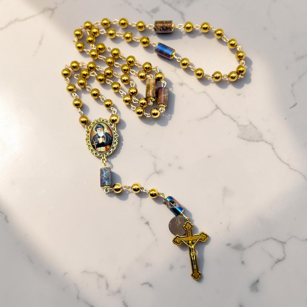 Handmade Gold St. Charbel Rosary arranged on marble background