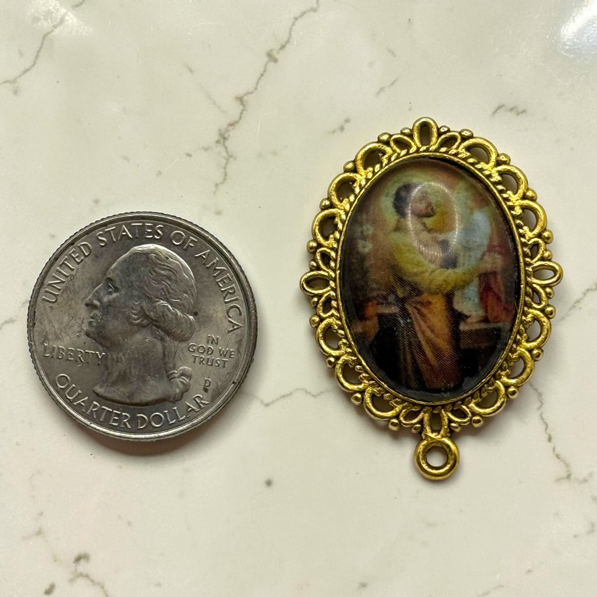 Gold St. Joseph and Child Jesus glass cabochon rosary centerpiece shown beside a quarter for scale