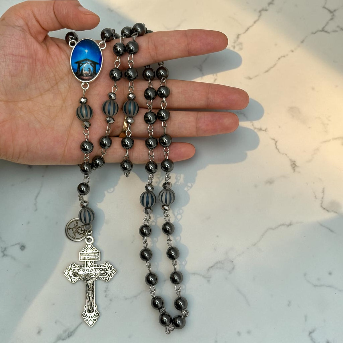 Hand holding handmade dark gray hematite Catholic rosary with striped glass beads and silver crucifix