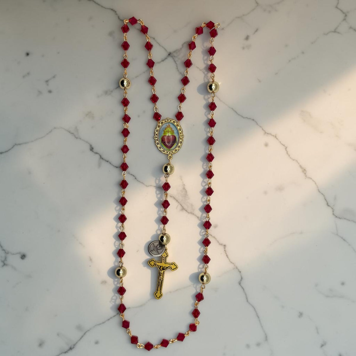 Red crystal Catholic rosary with gold-tone links, gold Our Father beads, Sacred Heart centerpiece, and gold crucifix