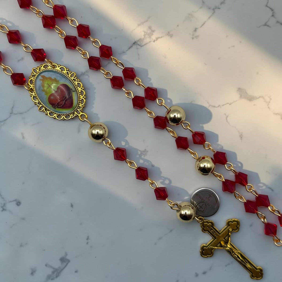 Close-up of red faceted crystal rosary with gold-tone beads, Sacred Heart centerpiece, and gold crucifix