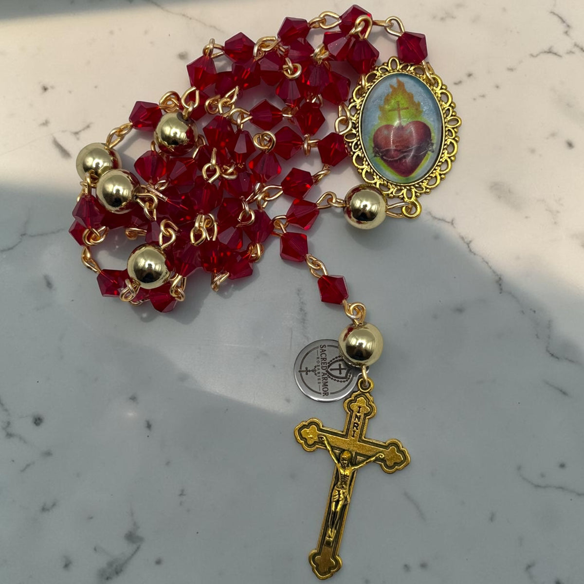 Red crystal Sacred Heart rosary arranged on marble with gold-tone crucifix and links