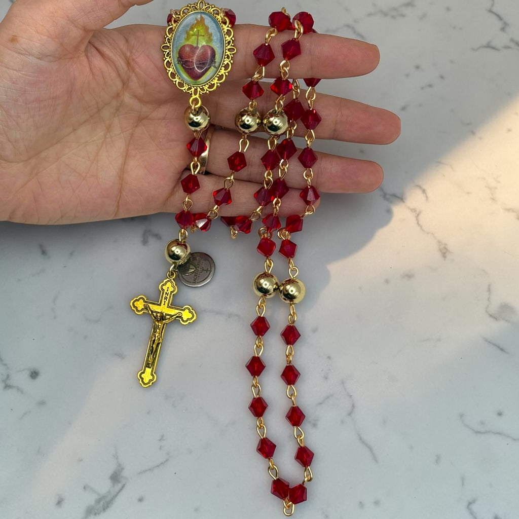 Hand holding red faceted crystal Sacred Heart rosary with gold-tone Our Father beads and crucifix