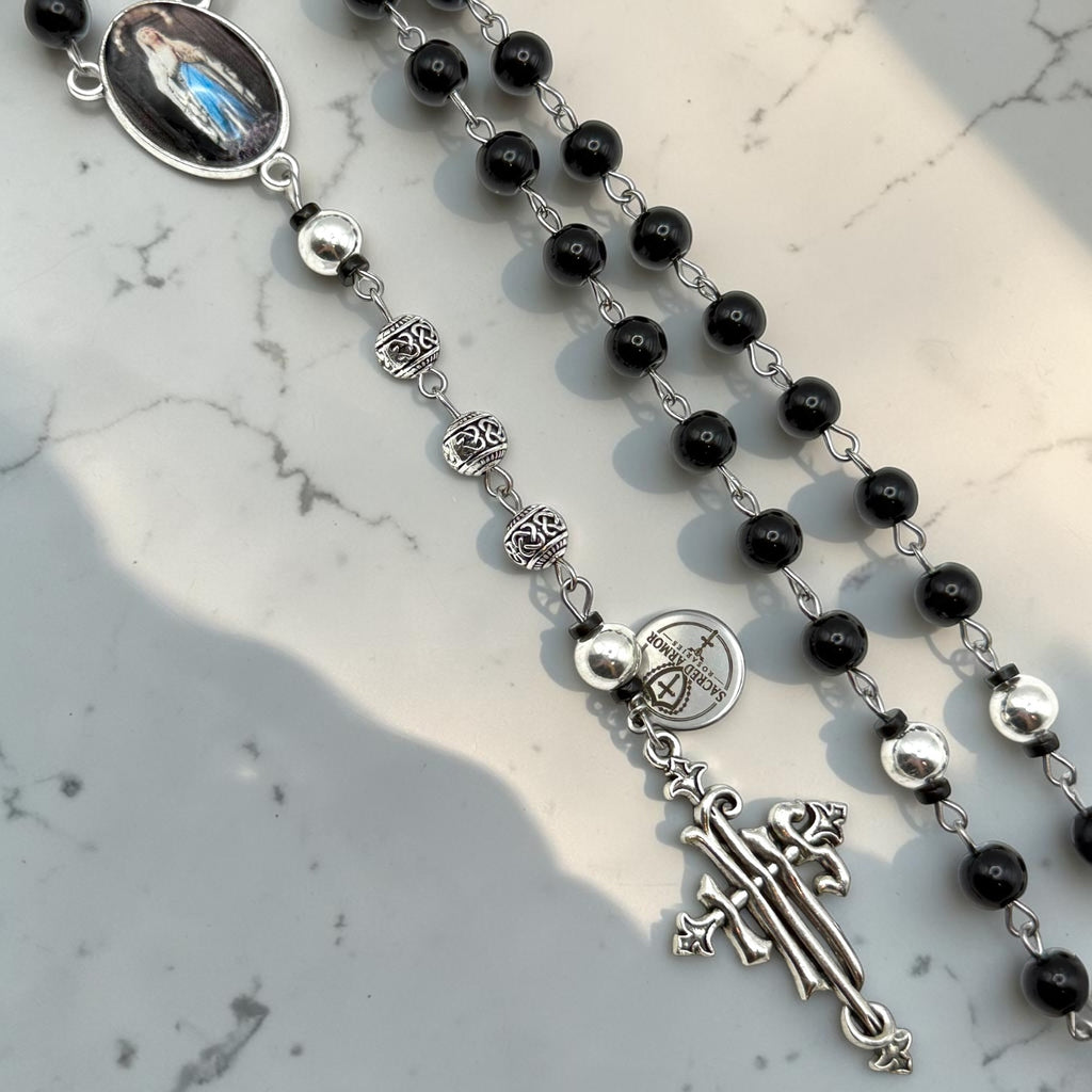 Close-up of black rosary with silver-tone Our Father beads, ornate accent beads, and silver crucifix