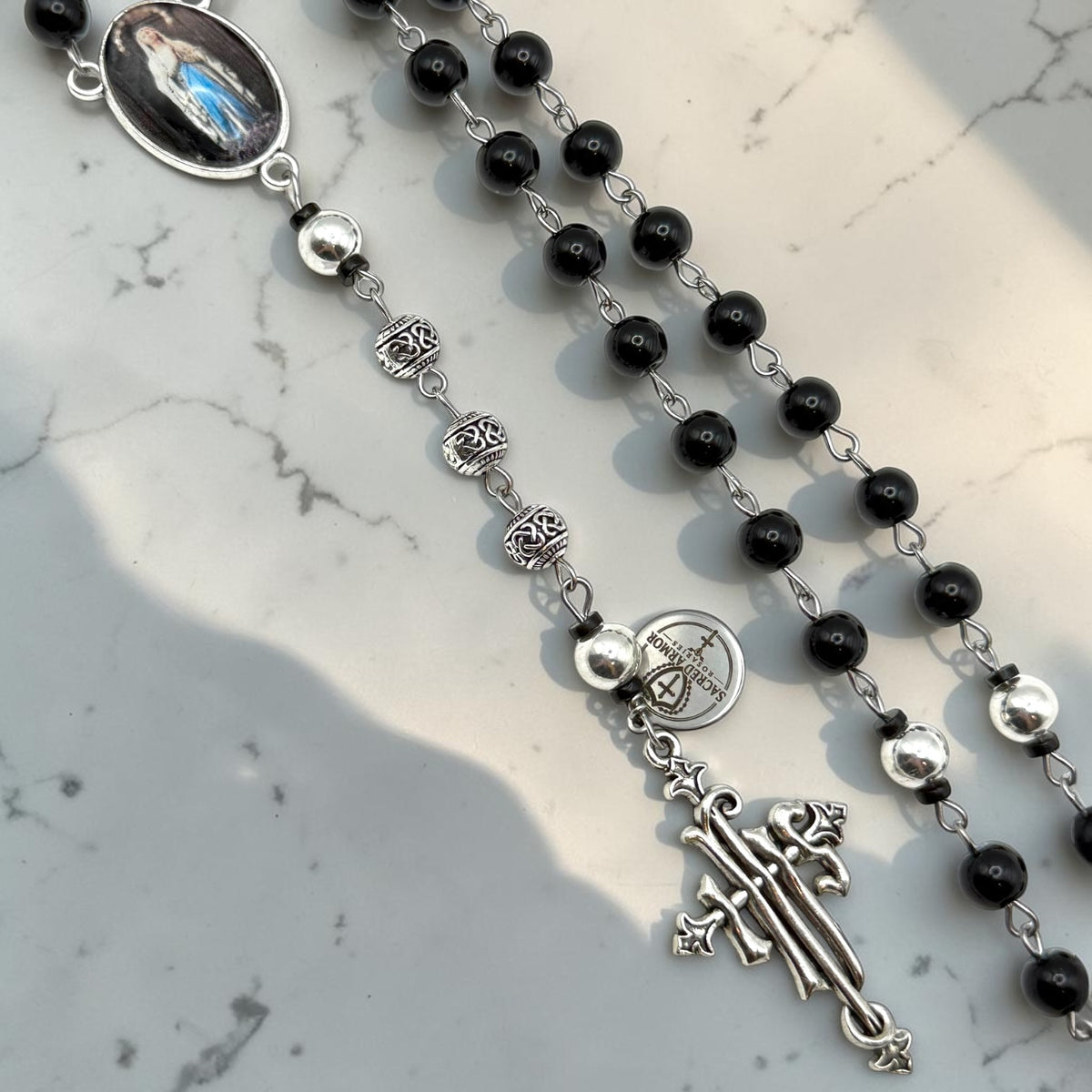 Close-up of black rosary with silver-tone Our Father beads, ornate accent beads, and silver crucifix