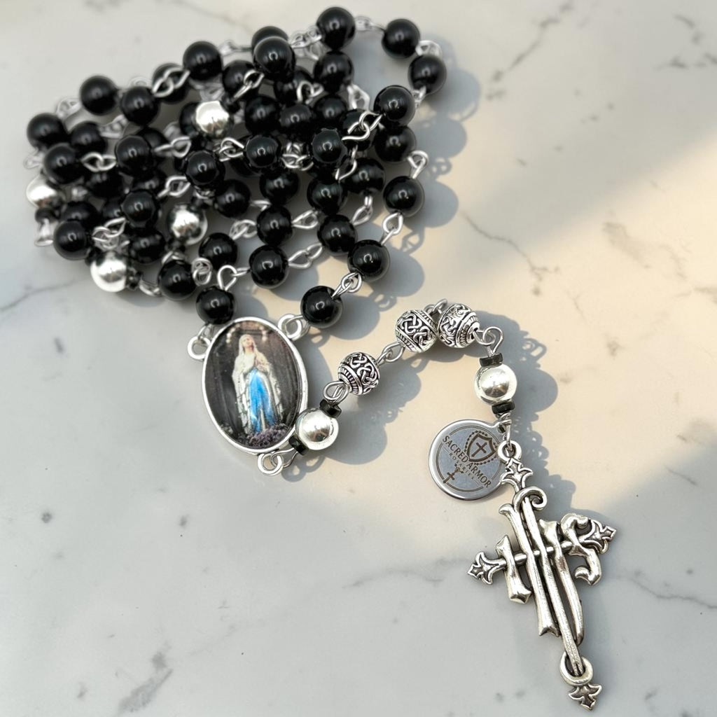 Our Lady of Lourdes black rosary arranged on marble with silver-tone centerpiece accents and ornate crucifix