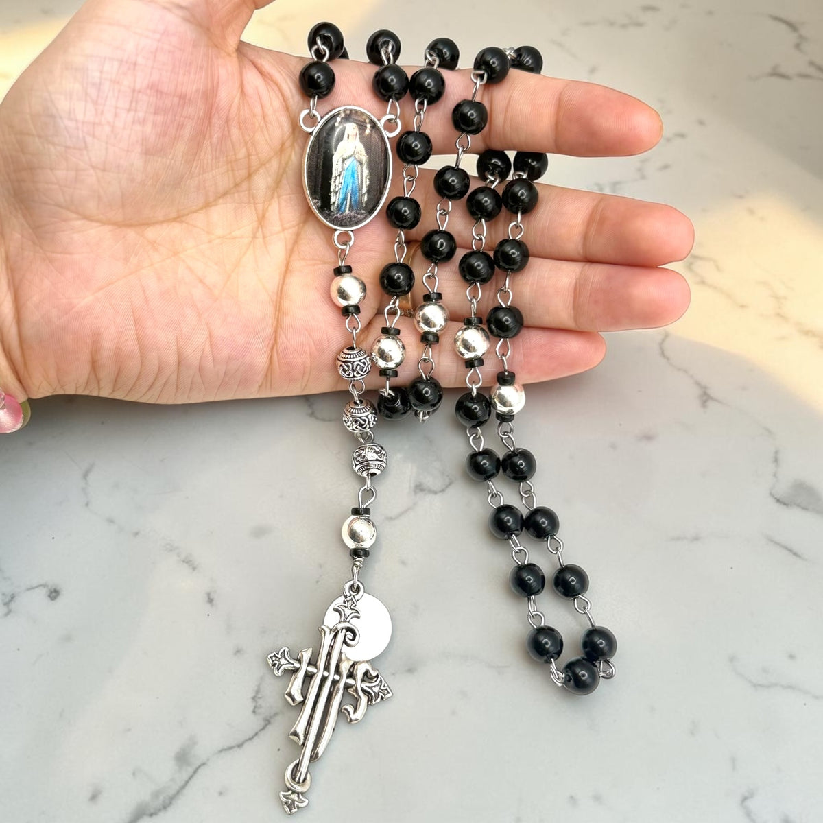Hand holding handmade black Our Lady of Lourdes rosary with silver-tone beads and ornate silver crucifix