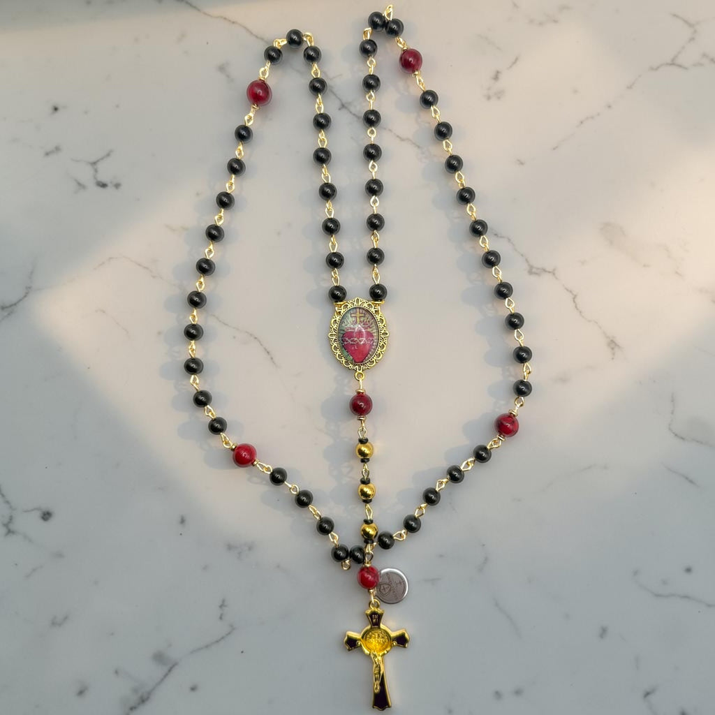 Black and red Catholic rosary with gold-tone links, Sacred Heart centerpiece, and purple-accented gold crucifix