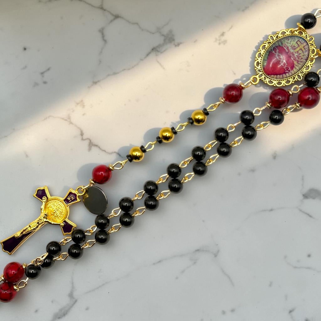 Close-up of black and red rosary with gold-tone accent beads, Sacred Heart centerpiece, and gold crucifix with purple accents