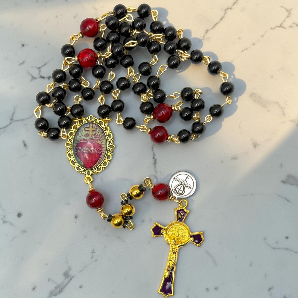 Handmade Sacred Heart rosary with glossy black beads, red accent beads, gold-tone links, and purple-accented crucifix
