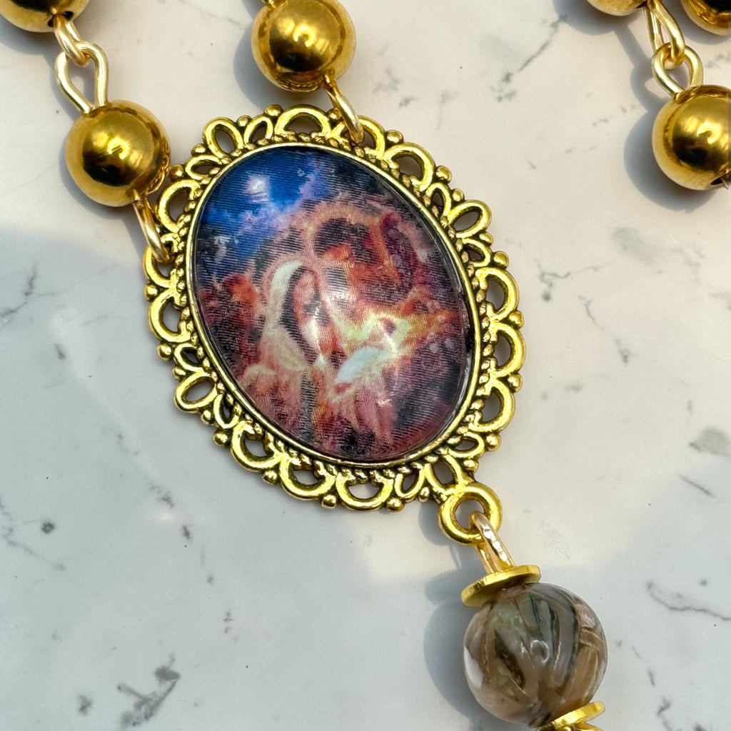 Close-up of ornate Holy Family devotional centerpiece on gold-tone rosary with polished gold beads