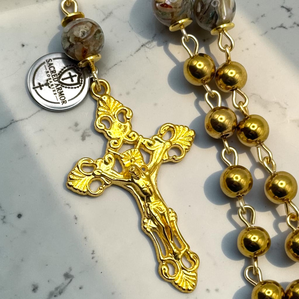 Close-up of ornate gold-tone crucifix and marbled glass Our Father bead on handmade Catholic rosary