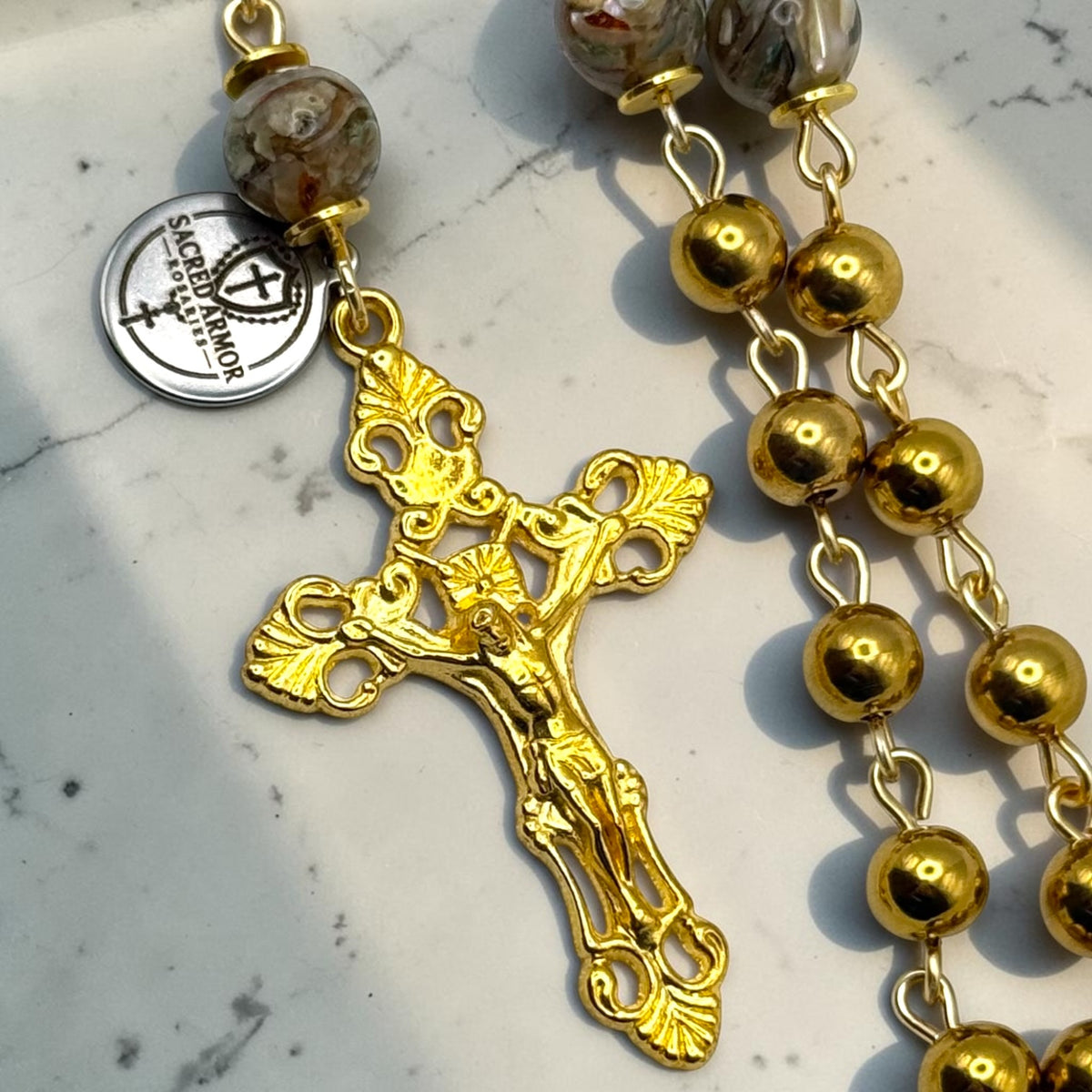 Close-up of ornate gold-tone crucifix and marbled glass Our Father bead on handmade Catholic rosary