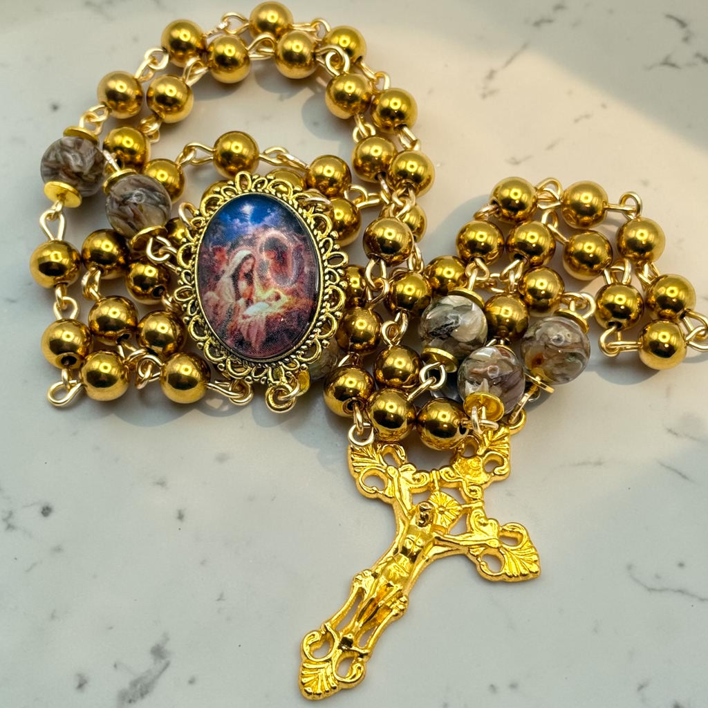 Gold-tone handmade rosary arranged on marble with ornate devotional centerpiece and gold crucifix