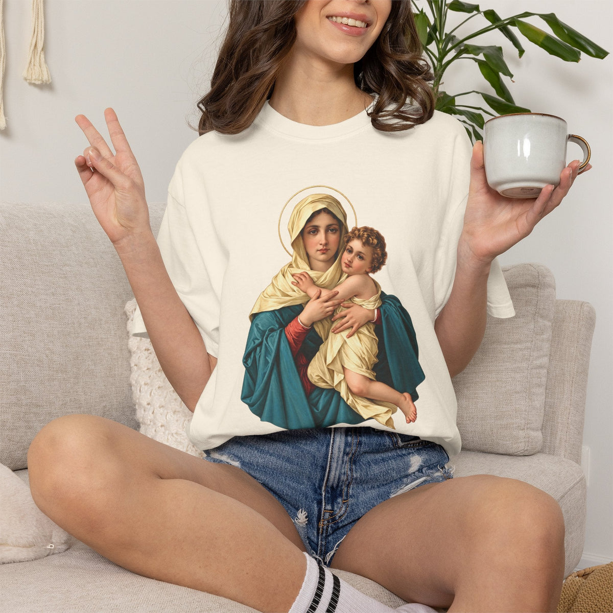 Sacred Armor Rosaries Comfort Colors t-shirt featuring Our Lady of Schoenstatt print on a woman sitting on a sofa