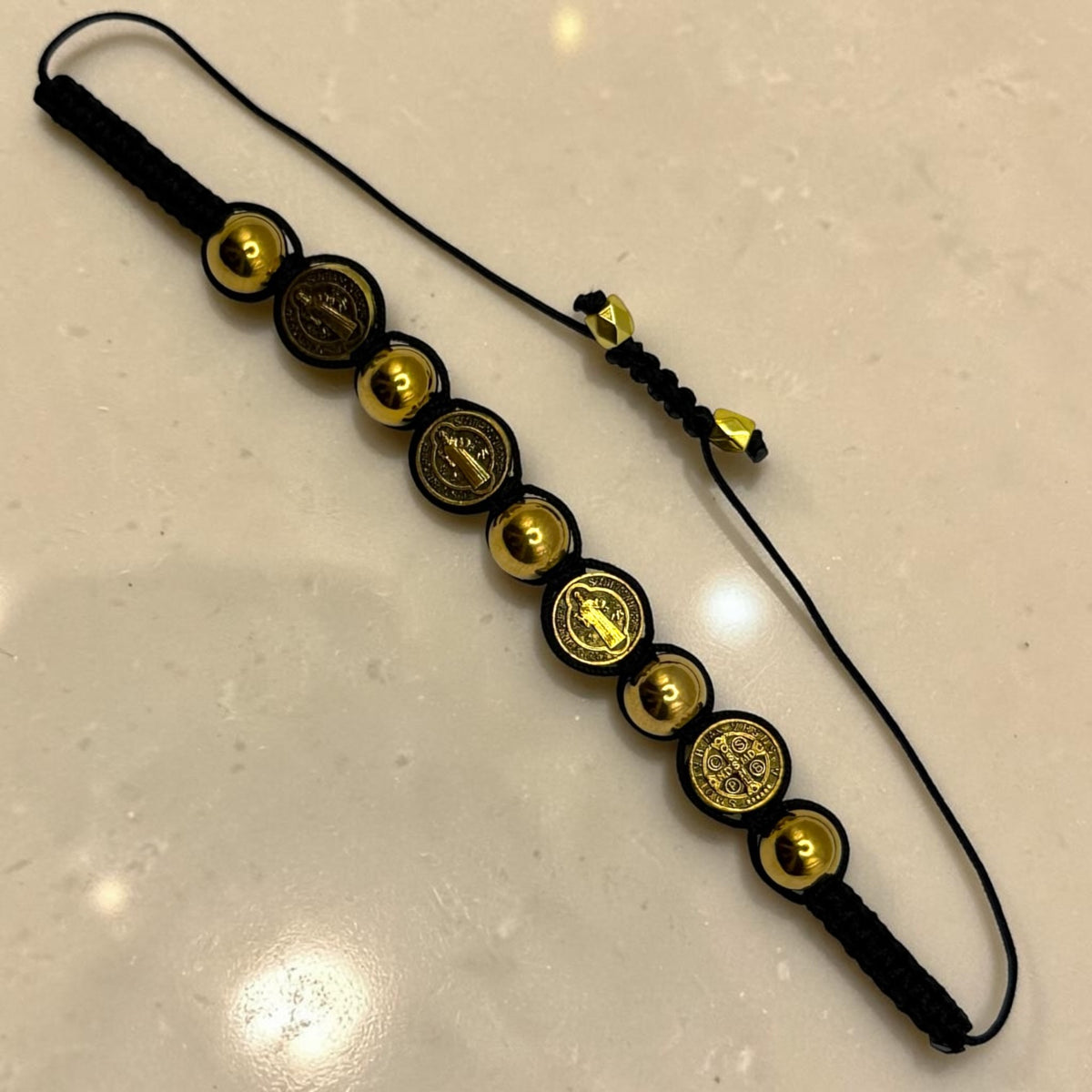 Gold and black St. Benedict medal bracelet laid flat