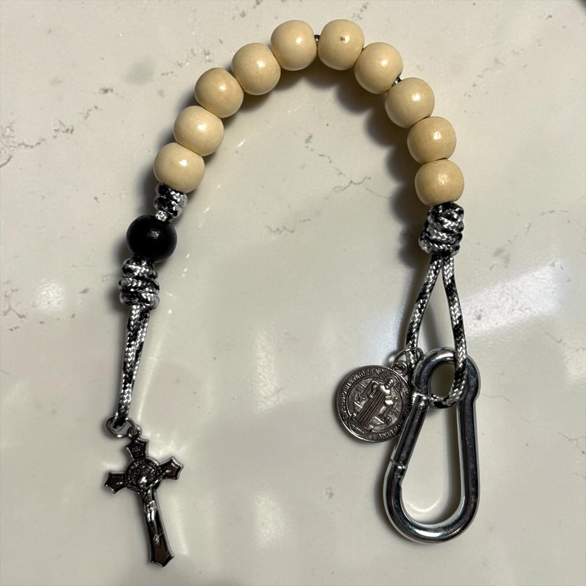 Close-up of white wood beads, black accent bead, silver-tone St. Benedict medal, carabiner, and crucifix on pocket decade rosary