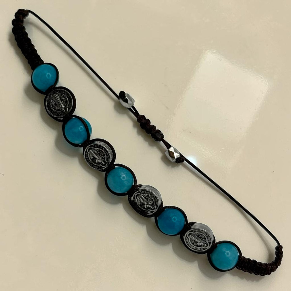 Adjustable turquoise-blue bead Saint Benedict medal bracelet laid flat